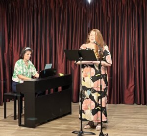 There are two women on the stage. One woman is playing the piano, the other one is singing