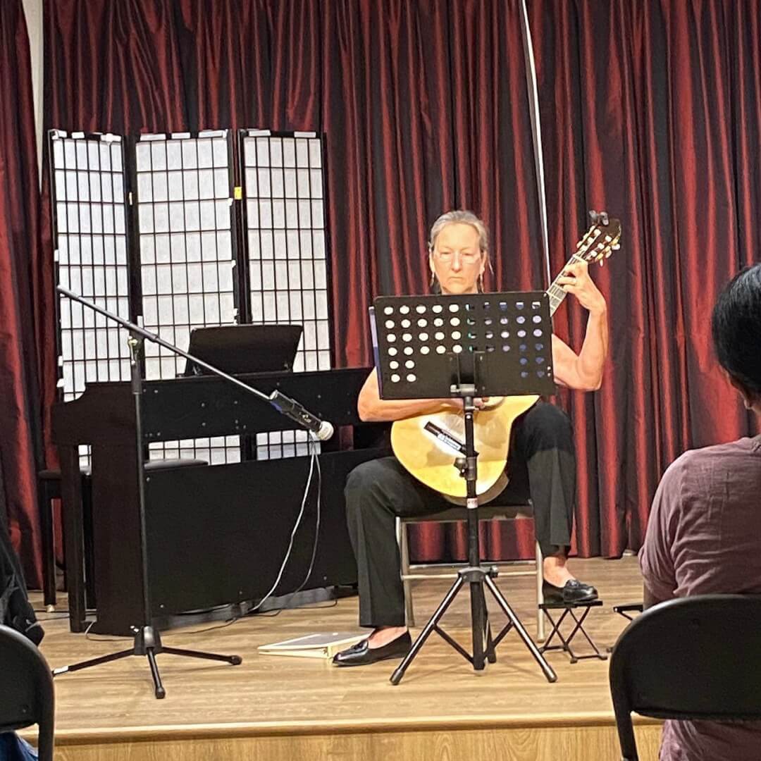 A woman is playing the guitar on the stage of assembly hall of CFA.
